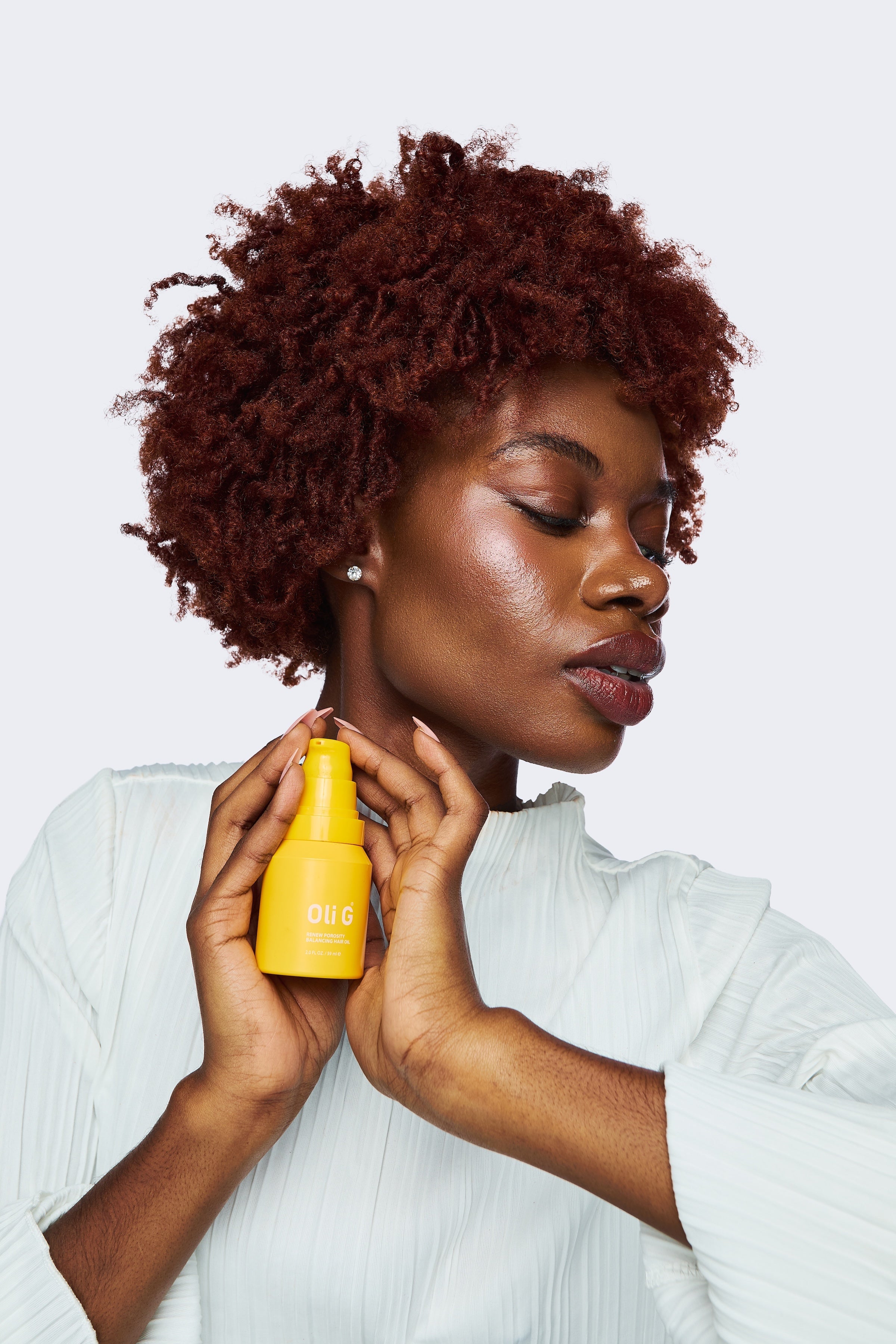 Model with coily red-brown hair holding Renew Porosity Balancing Oil